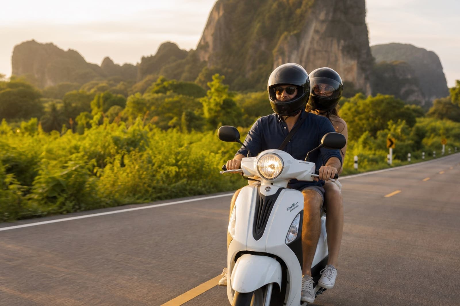 A couple riding together on one scooter through Krabi countryside, both wearing helmets