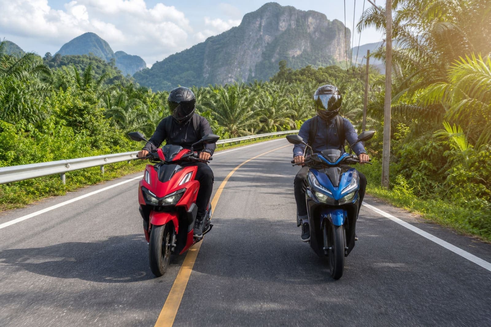 Two riders on separate scooters on a scenic country road in Krabi, both wearing helmets