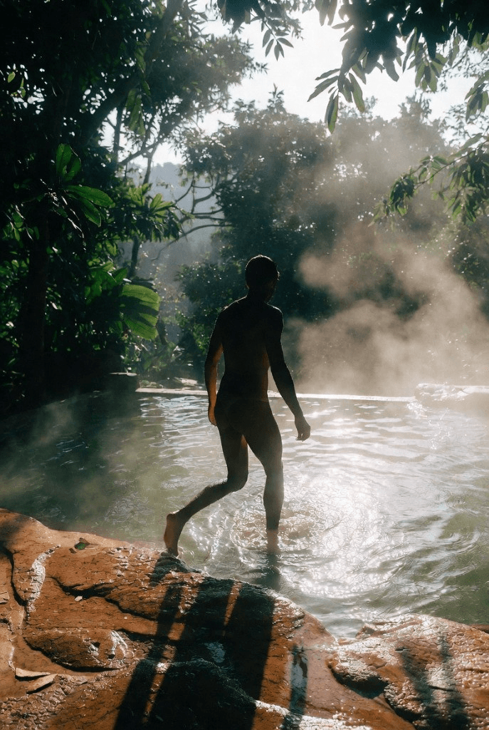 Visitor stepping into steaming hot spring pool at Krabi Hot Springs surrounded by jungle