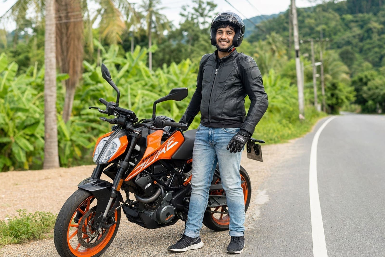 Rider in a leather jacket and full-face helmet standing beside a KTM Duke 390 on an open road