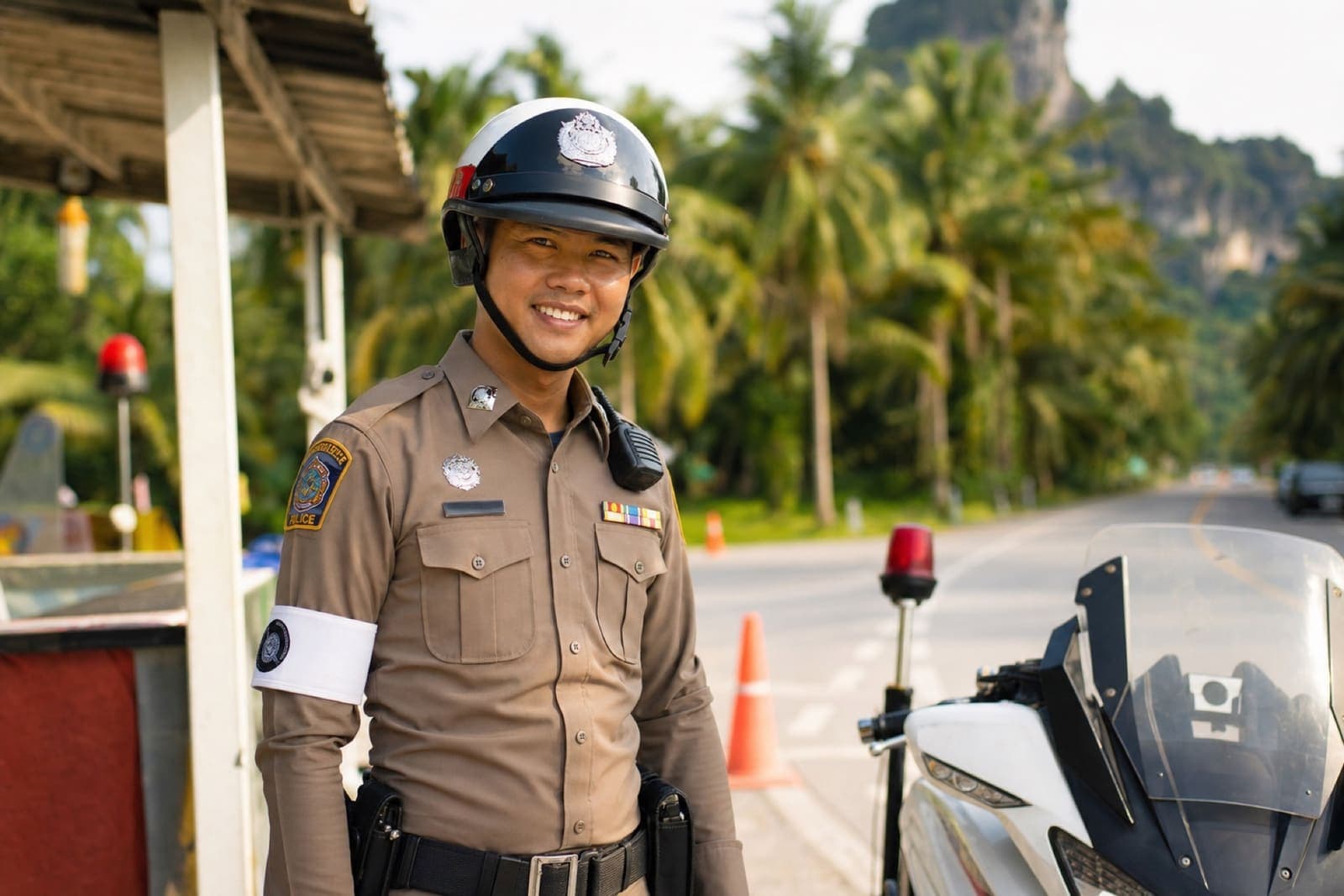 Smiling Thai police officer in standard Royal Thai Police uniform and issued white patrol helmet