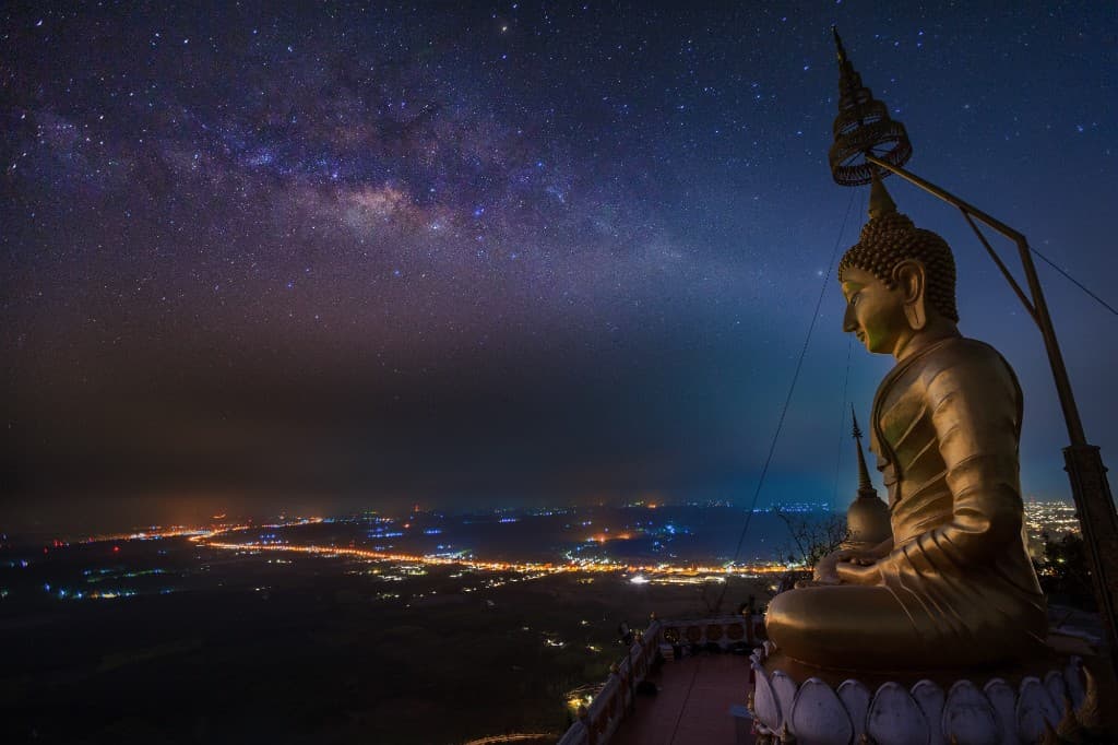 Golden Buddha at the summit of Tiger Cave Temple at night with Milky Way and Krabi city lights below