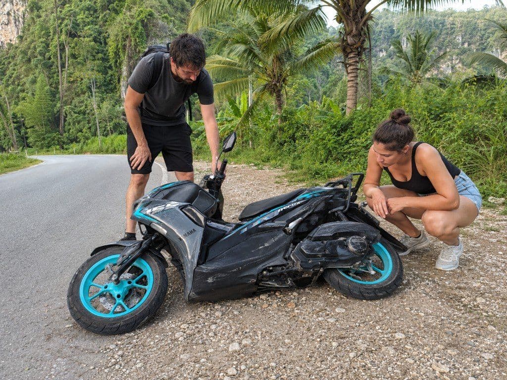 Couple inspecting a damaged Yamaha Aerox scooter on the roadside in Krabi after a fall
