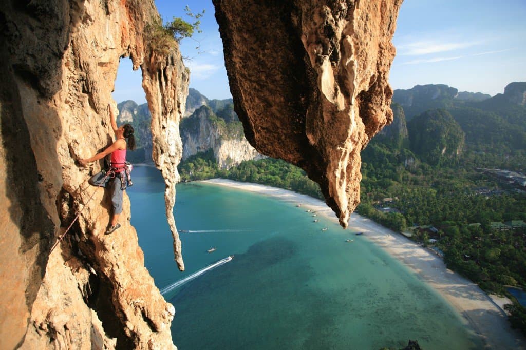 Rock climber on limestone cliffs above Railay West Beach and turquoise water, Krabi