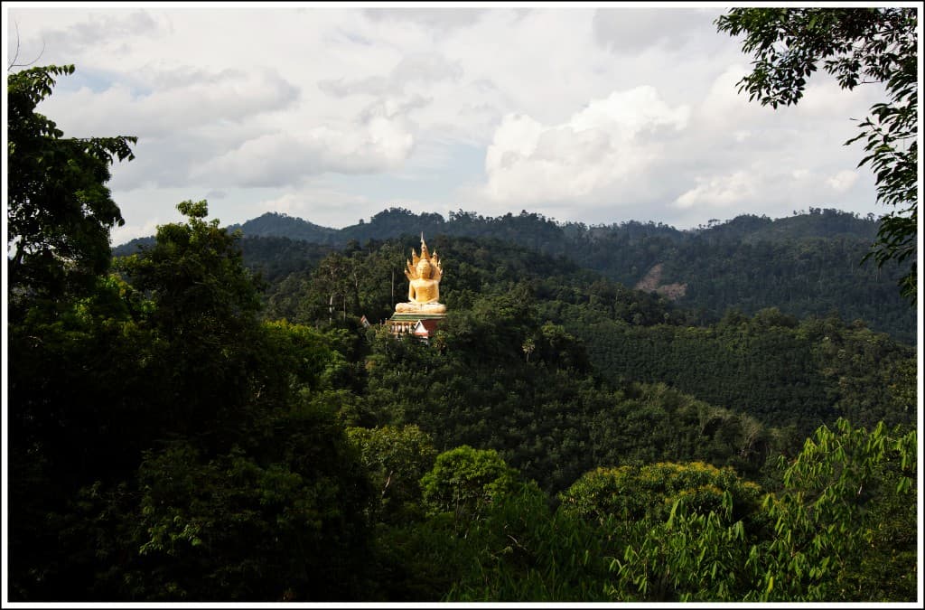 Golden Buddha statue among green hills at Wat Bang Riang, Krabi
