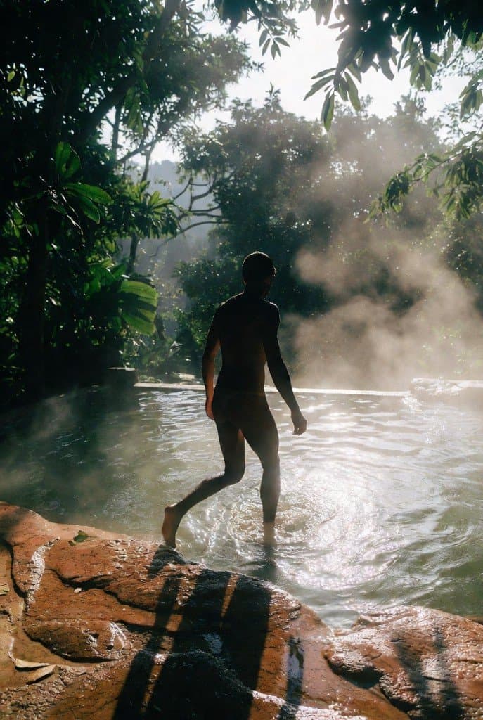 Visitor stepping into steaming hot spring pool at Krabi Hot Springs surrounded by jungle