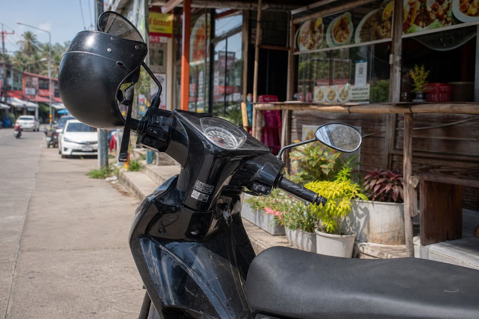 Helmet hanging on the mirror of a parked scooter outside a shop in Thailand