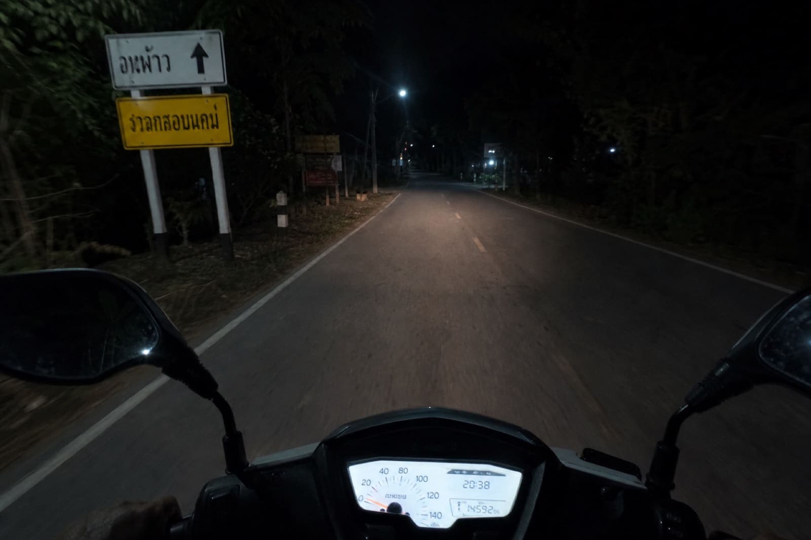 Dimly lit rural road in the Thai countryside at night seen from a slow scooter ride