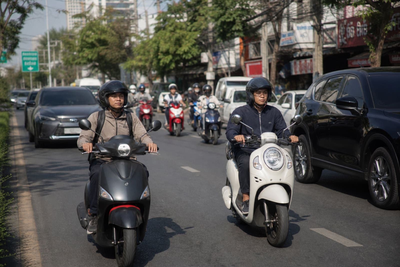 Scooter riders wearing helmets in calm Thailand traffic at a normal pace